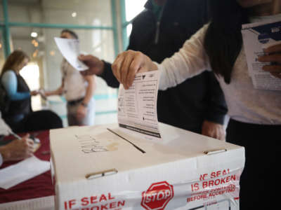 A voter puts a ballot into a ballot box