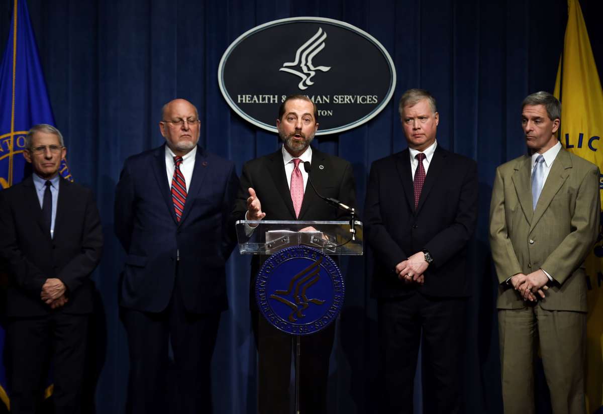 ﻿ Alex Azar speaks into a microphone at a podium surrounded by other men