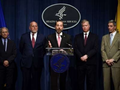  Alex Azar speaks into a microphone at a podium surrounded by other men