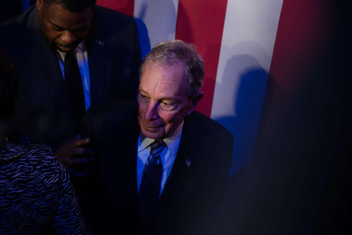 Mike Bloomberg stands in front of a U.S. flag flanked by supporters