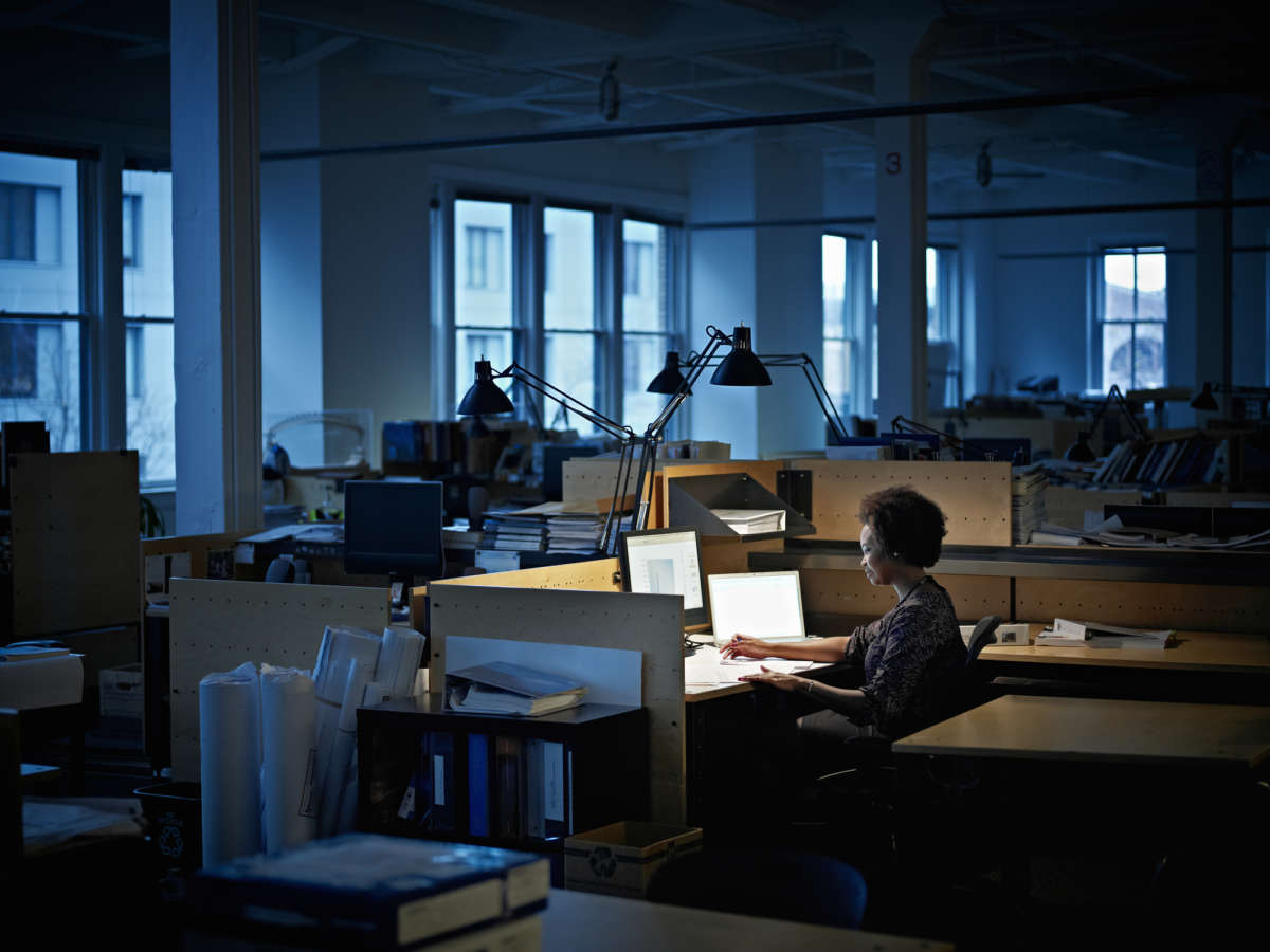 A woman sits at her desk alone in an empty and dark office