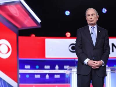 Mike Bloomberg stands to the left of the frame during a debate