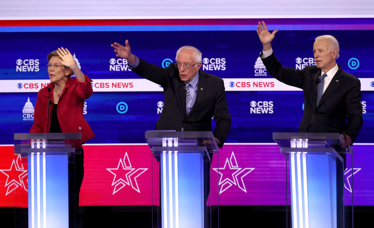 Sens. Elizabeth Warren and Bernie Sanders raise their hands alongside former Vice President Joe Biden during a debate