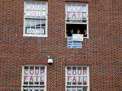 People display signs from within the windows of a brick building