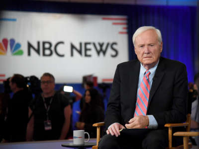 Chris Matthews sits in a chair in front of a sign reading "NBC NEWS"