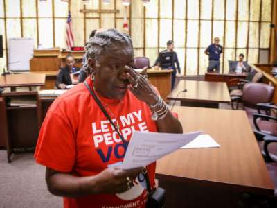 A woman cries in a courtroom while holding papers in one hand