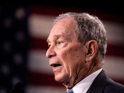 Mike Bloomberg, whose countenance looks remarkably similar to George W. Bush's in this photo, speaks in front of a U.S. Flag