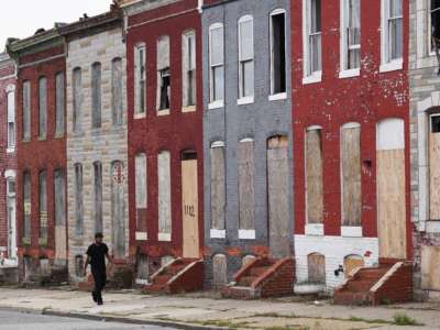 A pedestrian passes by a row of boarded up houses in east Baltimore, Maryland, on August 8, 2017.