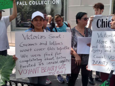 Women hold signs decrying sexual harassment at Voyant Beauty
