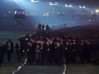 People dressed in black march in the fog by Auschwitz-Birkenau at night