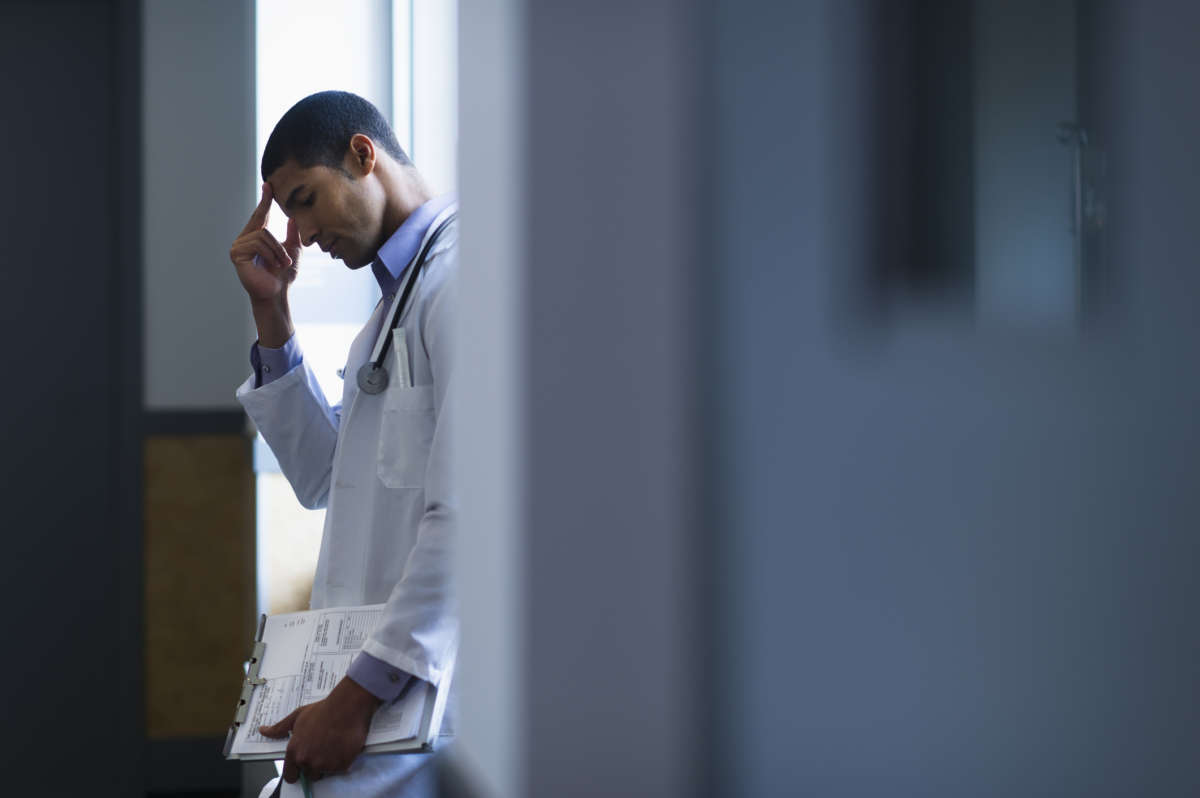 A doctor pinches the bridge of his nose in a hospital doorway