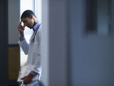 A doctor pinches the bridge of his nose in a hospital doorway