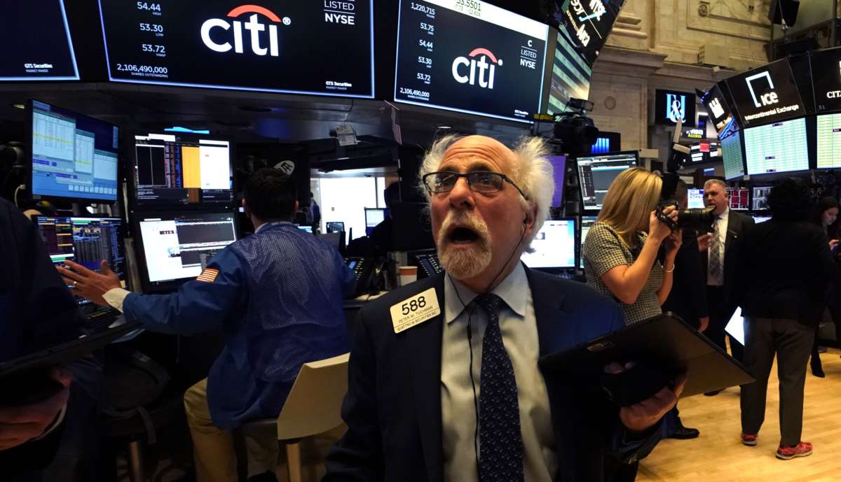 A white-haired stock broker looks on with horror at a screen in front of him