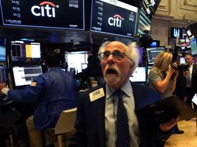 A white-haired stock broker looks on with horror at a screen in front of him
