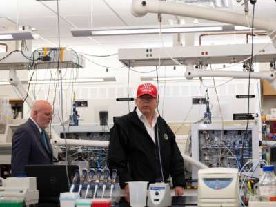 Donald Trump stands inside of a laboratory wearing a red maga hat