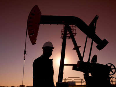 Silhouette of oil worker by pump jack on oil rig