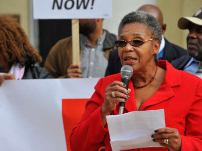 A woman wearing a red suit speaks into a microphone