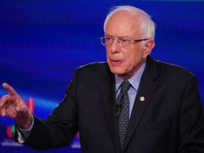 Bernie Sanders speaks in front of a blue screen bearing CNN's logo