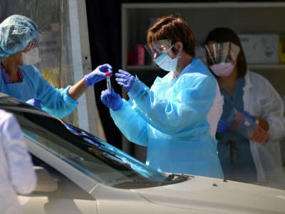 Medical workers at a Kaiser Permanente French Campus test a patient for the novel coronavirus, COVID-19, at a drive-thru testing facility in San Francisco, California, on March 12, 2020.