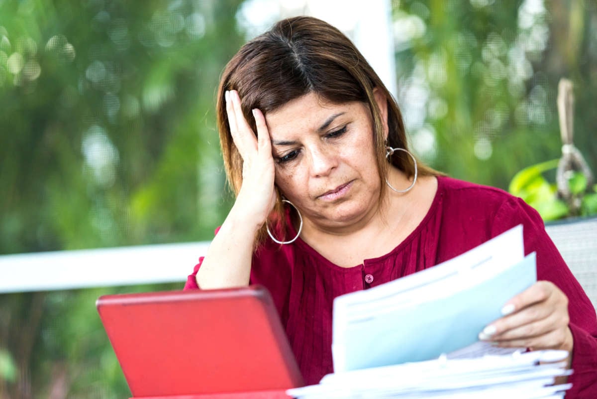 A woman holds her head and looks at bills