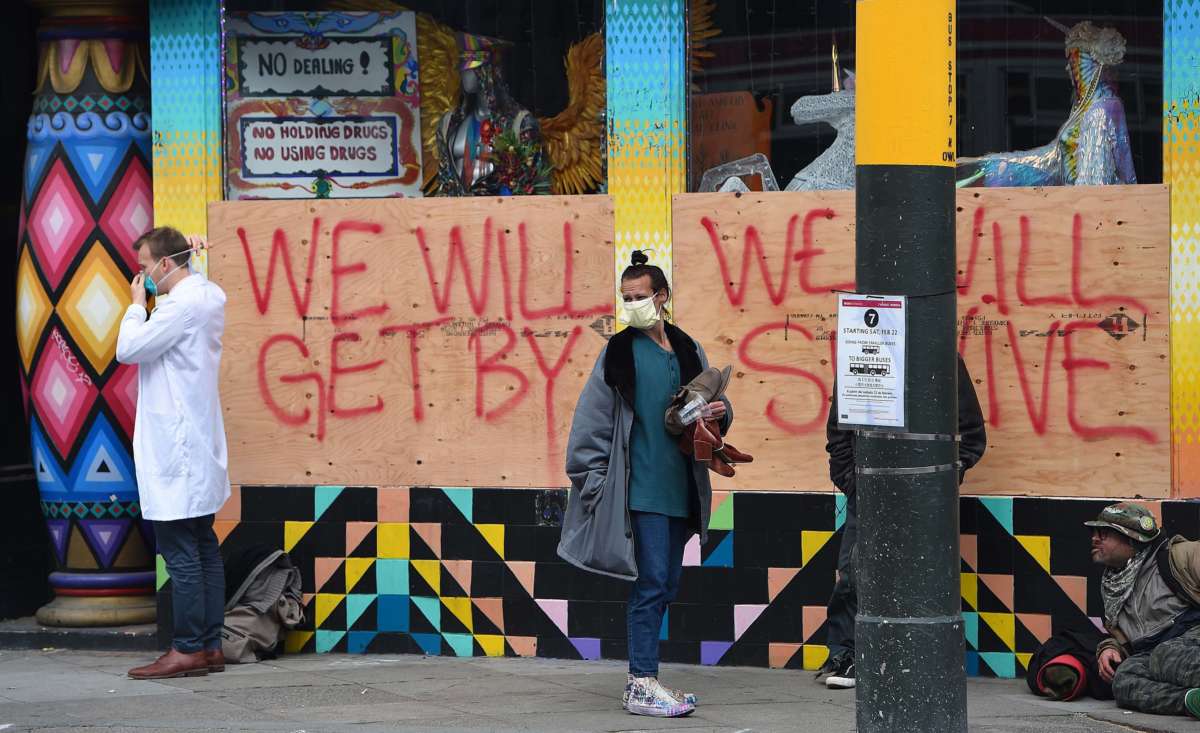 Stuart Malcolm, left, a doctor with the Haight Ashbury Free Clinic, puts on a mask before speaking with homeless people about the coronavirus in front of a boarded-up shop in the Haight Ashbury area of San Francisco, California, on March 17, 2020.
