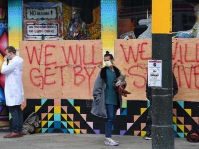 Stuart Malcolm, left, a doctor with the Haight Ashbury Free Clinic, puts on a mask before speaking with homeless people about the coronavirus in front of a boarded-up shop in the Haight Ashbury area of San Francisco, California, on March 17, 2020.