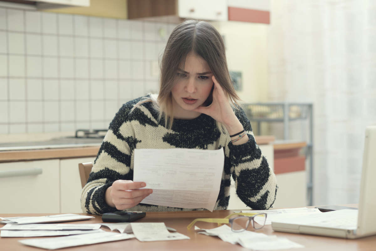 A woman looks at bills in her hand in shock