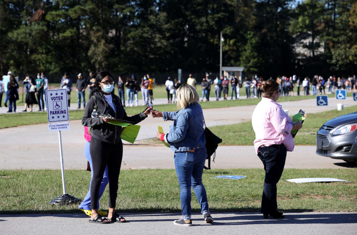 A poll worker hands out pens and clipboards to fill out registration cards as people stand in line to vote at the Gwinnett County Fairgrounds on October 30, 2020, in Lawrenceville, Georgia.
