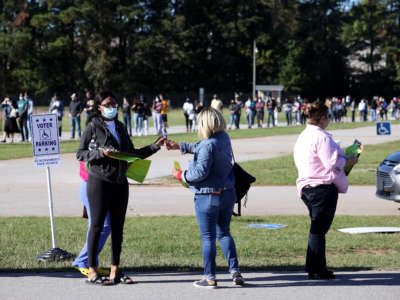 A poll worker hands out pens and clipboards to fill out registration cards as people stand in line to vote at the Gwinnett County Fairgrounds on October 30, 2020, in Lawrenceville, Georgia.