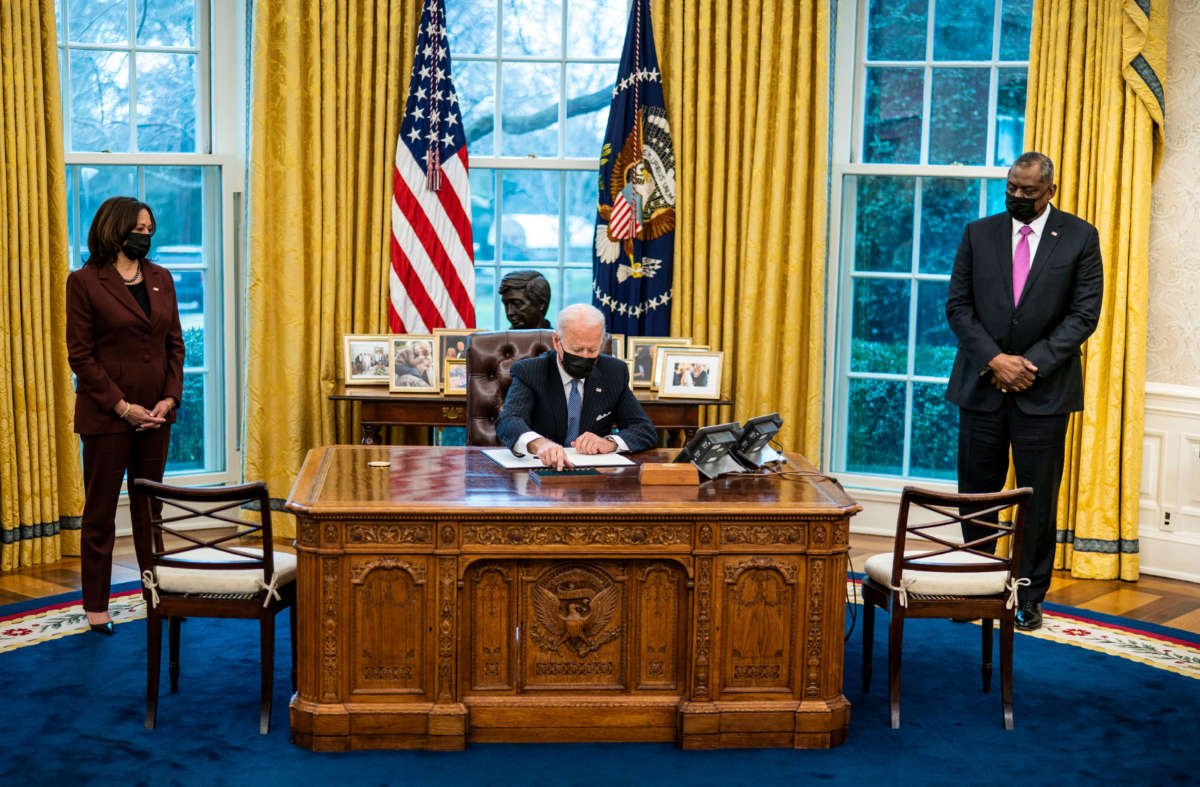 Flanked by Vice President Kamala Harris and Secretary of Defense Lloyd Austin, President Joe Biden signs an executive order in the Oval Office of the White House on January 25, 2021 in Washington, D.C.