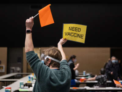 A Virgina Mason advanced registered nurse practitioner holds up a sign and a flag asking for another patient to dose with the Pfizer Covid-19 vaccine as well as a refill during a partnership with the hospital network and Amazon at the Amazon Meeting Center in downtown Seattle, Washington, on January 24, 2021.