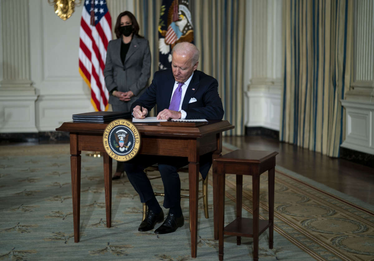President Joe Biden signs an executive order as Vice President Kamala Harris stands awkwardly in the background