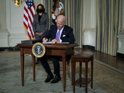 President Joe Biden signs an executive order as Vice President Kamala Harris stands awkwardly in the background