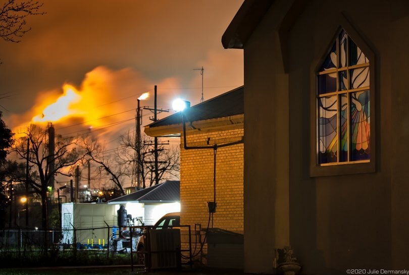 Firey plumes burn from a refinery behind a church