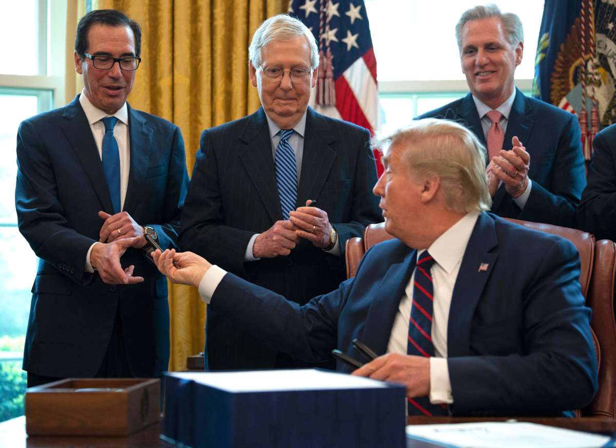 Donald Trump hands out pens to Treasury Secretary Steven Mnuchin and Senate Majority Leader Mitch McConnell after signing the Coronavirus Aid, Relief, and Economic Security (CARES) Act, a $2 trillion rescue package to provide economic relief amid the coronavirus outbreak, at the Oval Office of the White House on March 27, 2020.