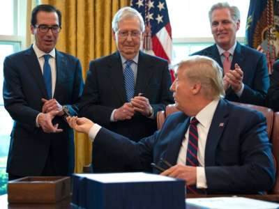 Donald Trump hands out pens to Treasury Secretary Steven Mnuchin and Senate Majority Leader Mitch McConnell after signing the Coronavirus Aid, Relief, and Economic Security (CARES) Act, a $2 trillion rescue package to provide economic relief amid the coronavirus outbreak, at the Oval Office of the White House on March 27, 2020.