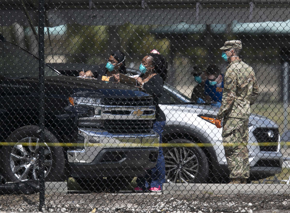 soldiers in blue face masks observe people filling out paperwork