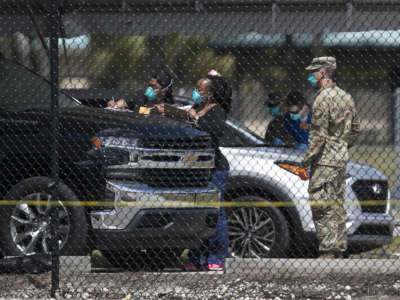 soldiers in blue face masks observe people filling out paperwork