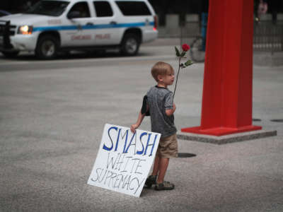 A young boy holds a sign reading "SMASH WHITE SUPREMACY" in one hand and a rose in the other during a protest