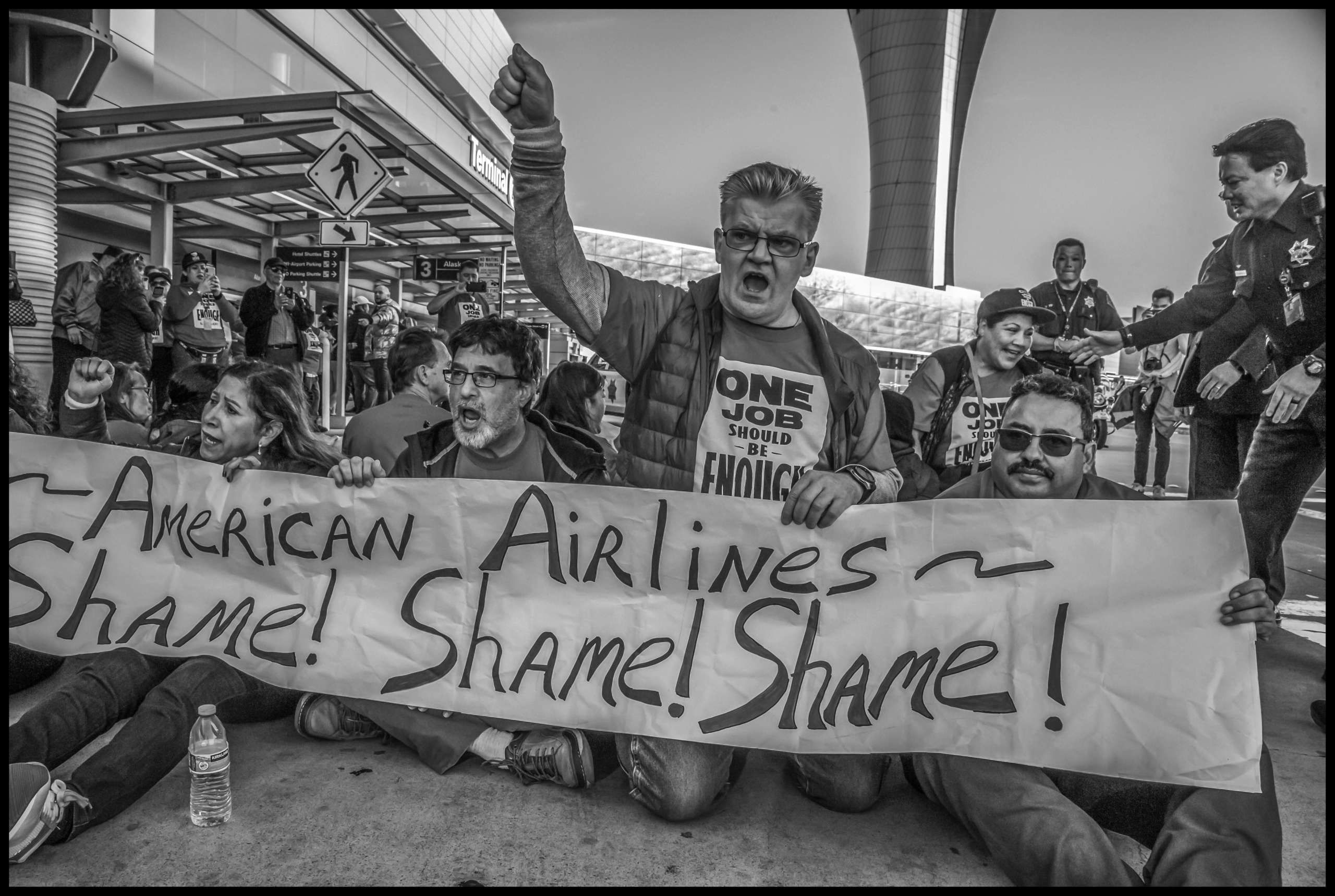 As they prepare to be arrested, workers hold a banner shaming American Airlines.