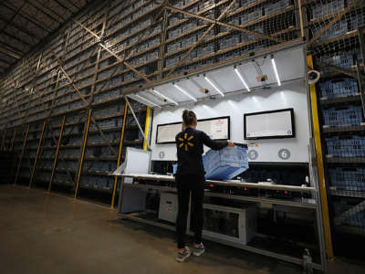 A walmart employee holds a box in a warehouse