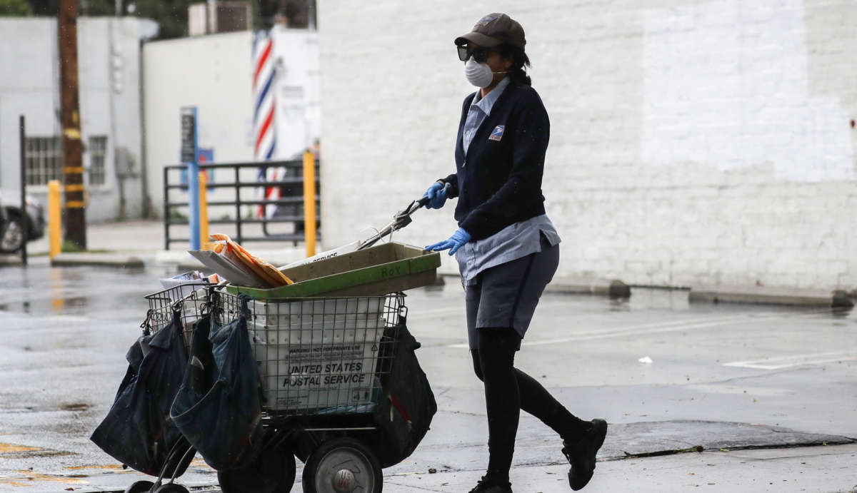 A U.S. Postal Service worker wears a mask and gloves while delivering mail near a Food Bank distribution for those in need, as the coronavirus pandemic continues, on April 9, 2020, in Van Nuys, California.