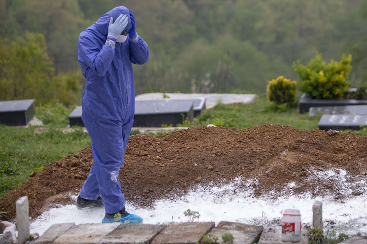 A person in a hazmat suit looks down upon a mass grave in despair