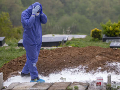 A person in a hazmat suit looks down upon a mass grave in despair