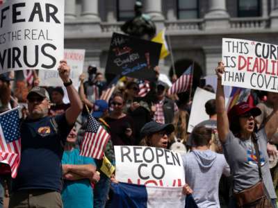 A bunch of people displaying the US flag protest outside a statehouse