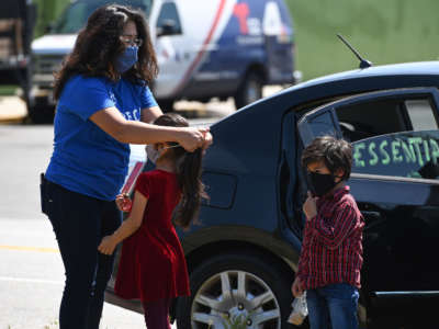 Activist Michelle Lozano puts a mask on her children Maya and Iker as day laborers and their supporters participate in a "Caravan for Essential and Excluded Workers" in Los Angeles, California, on April 14, 2020. The caravan calls on California Gov. Gavin Newsom to ensure that COVID-19 related emergency financial aid from the federal CARES Act reaches day laborers, undocumented workers and their families.