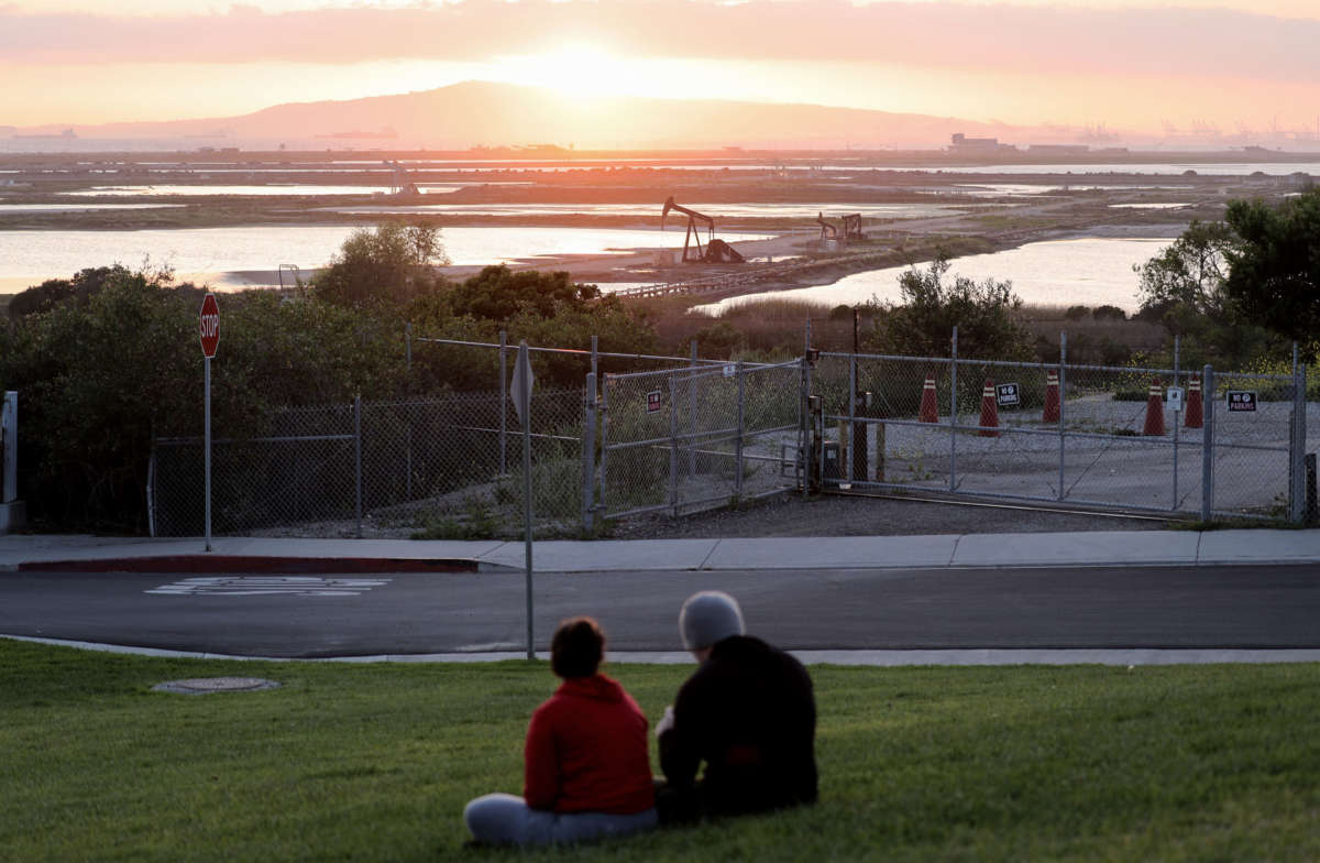 People sit on a hillside overlooking oil pumpjacks at the Huntington Beach Oil Fields amidst the coronavirus pandemic on April 20, 2020, in Huntington Beach, California. Oil prices traded in negative territory for the first time as the spread of COVID-19 impacts global demand.