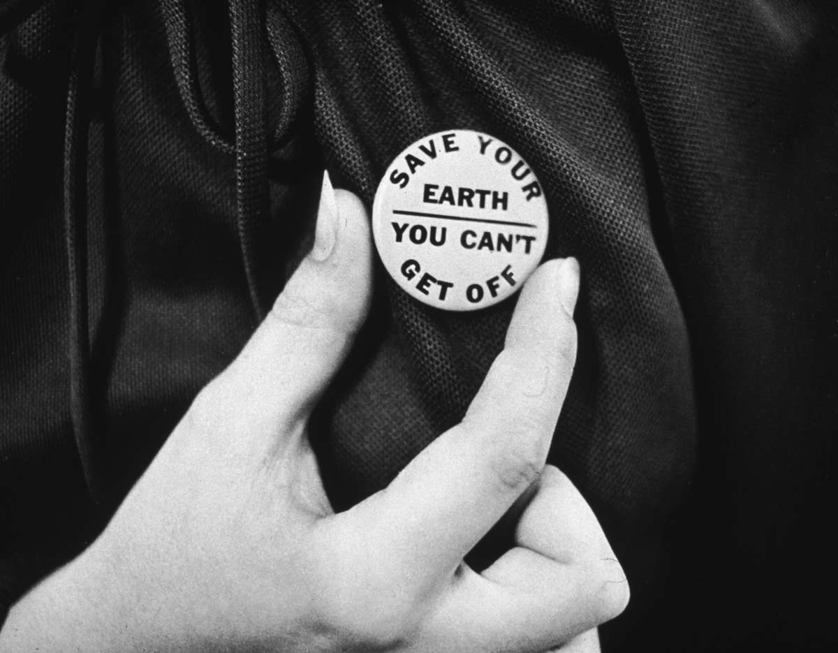 A protester adjusts a button reading "SAVE YOUR EARTH; YOU CAN'T GET OFF"