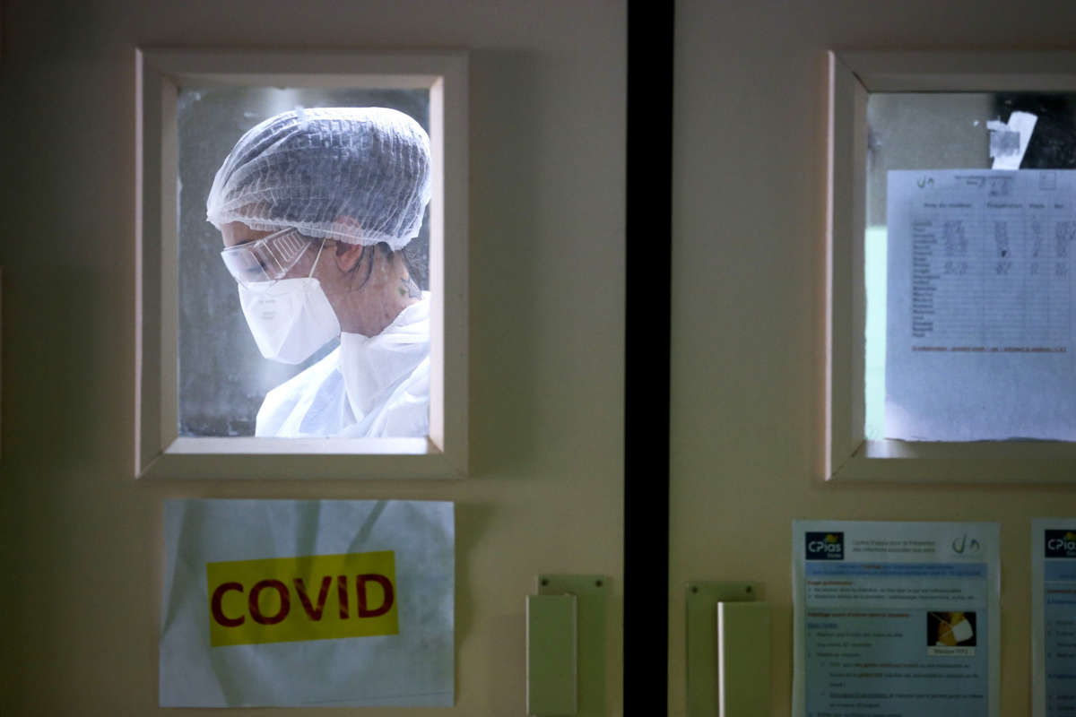 A nurse in protective gear is seen through the window in a hospital door