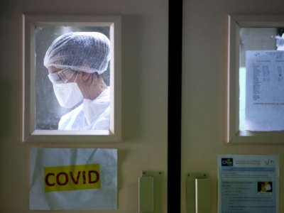 A nurse in protective gear is seen through the window in a hospital door